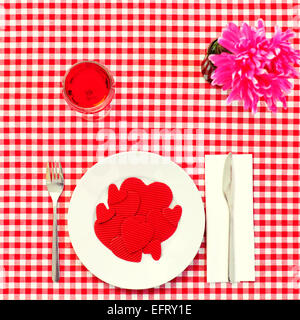 Capture d'un grand angle d'une assiette pleine de coeurs rouges de différentes tailles sur un ensemble table avec une nappe blanche et rouge à carreaux Banque D'Images