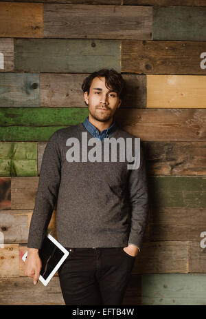 Portrait of young businessman with a digital tablet debout contre un mur en bois. Beau jeune détendu en comité permanent du conseil exécutif Banque D'Images