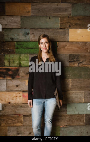 Portrait of attractive young woman standing contre un mur en bois. Caucasian woman in casuals dans office looking at camera. Banque D'Images