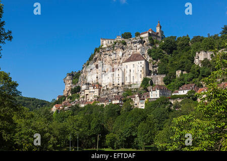 Bâtiments à flanc de falaise de Rocamadour, Dordogne, en France, en regardant vers le haut de la vallée ci-dessous entouré d'arbres en feuilles contre un ciel bleu clair Banque D'Images