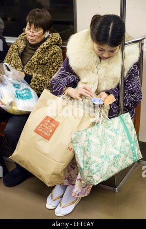 Les jeunes femmes sur leurs téléphones intelligents avec leurs achats dans le métro. Tokyo, Japon Banque D'Images