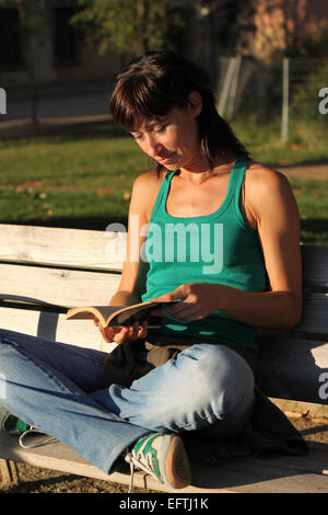 Fille assise sur le banc de parc au soleil, lire un livre, dans le Parc de la Ciutadella, Barcelone, Catalogne, Espagne Banque D'Images