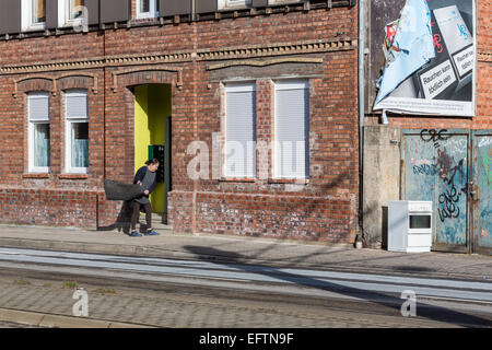 Une femme dans une rue de nettoyer un tapis en tapant contre le mur à l'extérieur de sa maison Banque D'Images