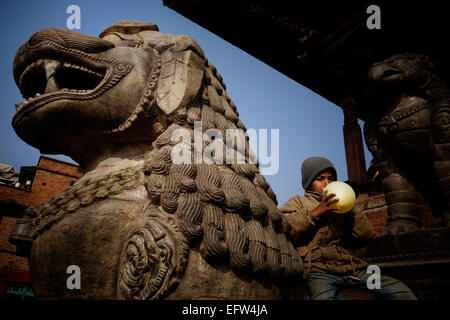 Un jeune garçon de gonfler un ballon et assis sur un lion sculpté dans le temple de Nyatapola népalais érigés par le roi Bhupatindra Malla en 1702 dans la ville de Bhaktapur, également connu sous le nom de Khwopa au Népal Banque D'Images