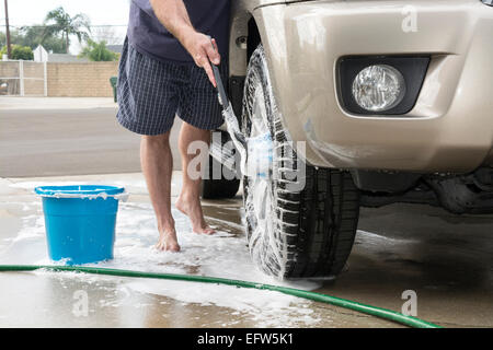 Un homme lave sa voiture utilise une brosse savonneuse pour nettoyer les pneus et les roues de son véhicule. Banque D'Images