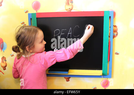 Petite fille écrit sur tableau noir mot Paix Banque D'Images