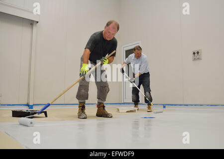 Deux commerçants roll une seconde couche d'époxy teintée produit sur le plancher d'un bâtiment industriel Banque D'Images