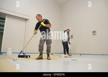 Deux commerçants roll une seconde couche d'époxy teintée produit sur le plancher d'un bâtiment industriel Banque D'Images