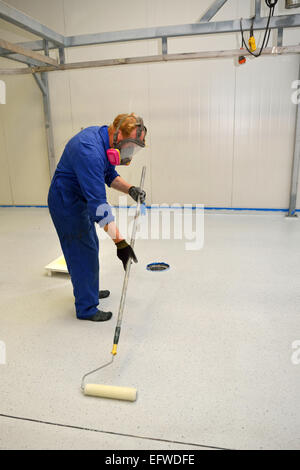 Un commerçant rolls une couche finale d'époxy clair produit sur le plancher d'un bâtiment industriel Banque D'Images