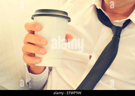 Un jeune homme avec sa cravate desserrée de boire du café dans une tasse de papier Banque D'Images