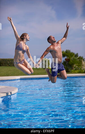 Jeune couple qui saute dans la piscine en vacances Banque D'Images