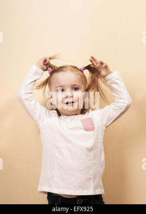 Peu playful girl holding her queues, vertical studio portrait Banque D'Images