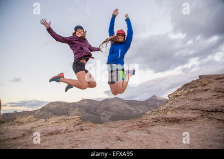 Deux jeunes femmes alpinistes jumping mid air sur haut de Smith Rock, Oregon, USA Banque D'Images