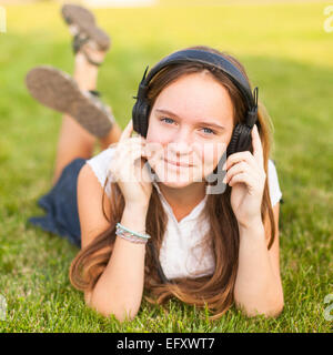 Jeune fille dans les écouteurs jouit de la musique allongé sur l'herbe verte. Banque D'Images
