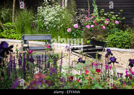 Sièges en cuir noir sur la terrasse en pierre avec lit fait de pierres et de frontières avec la plantation naturaliste Banque D'Images