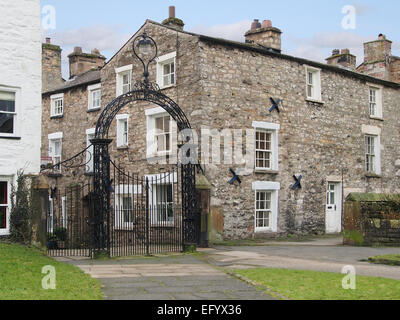 Portes en fer forgé de l'église Sainte Marie de Kirkby Lonsdale, une ville dans la région de Cumbria, montrant les cottages traditionnels en pierre. Banque D'Images