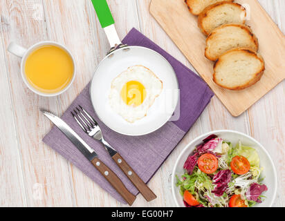 Petit-déjeuner sain avec œuf frit, toasts et salade sur table en bois blanc Banque D'Images