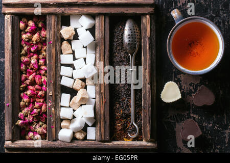 Ensemble de thé, thé noir sec roses et des morceaux de sucre dans un coffret en bois avec plateau vintage crépine et tasse de thé Banque D'Images