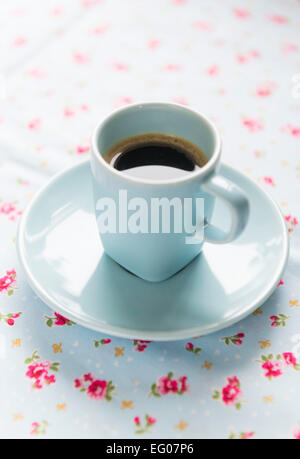 Machine à café expresso dans une tasse et soucoupe bleue sur un tableau floral chiffon. Banque D'Images