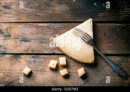 Gros morceau et de petits cubes de fromage belge avec vintage fourchette sur fond de bois. Vue d'en haut. Banque D'Images