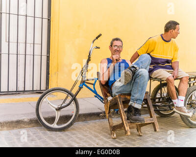 Location de deux hommes s'asseoir près de leur livraison 3 roues vélos livraison contre un mur jaune et parler à La Havane, Cuba, Vieja. Banque D'Images