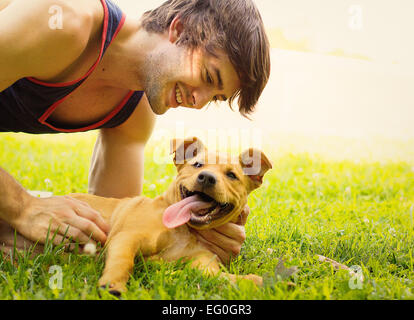 Smiling man lying on grass caresser son chiot chien Banque D'Images