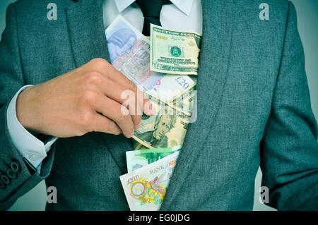 Man in suit mettre euro, dollar et livre des projets de loi à sa veste, illustrant des concepts tels que la cupidité, la corruption ou misappropri Banque D'Images