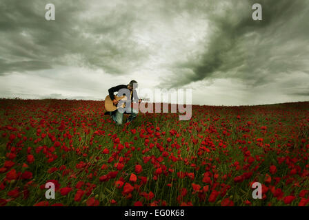 Homme jouant de la guitare dans champ de coquelicots Banque D'Images