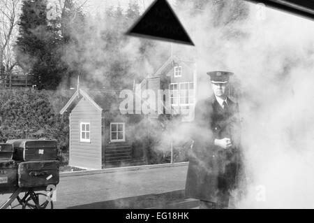 Image en noir et blanc regardant par une fenêtre de chariot de chemin de fer à un maître de gare englouti en vapeur debout sur la plate-forme Banque D'Images