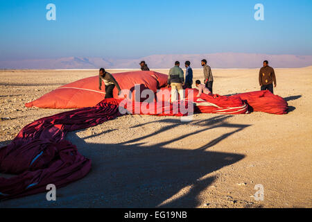 L'enveloppe rouge d'un ballon à air chaud au débarquement est dégonflé et plié sur la rive ouest du Nil en Egypte. Banque D'Images