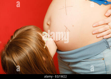 Grossesse, maternité et de bonheur concept. femme enceinte avec smiley heureux peint sur le ventre et sa fille peu Banque D'Images