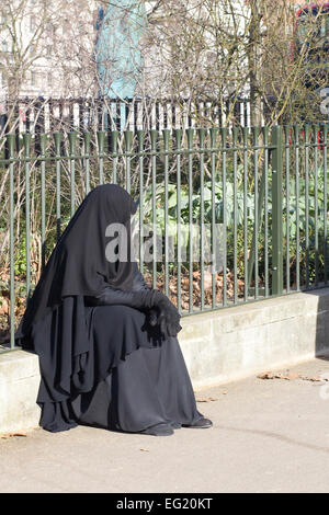 Femme musulmane dans une burqa assis sur le trottoir à Londres, Angleterre Banque D'Images