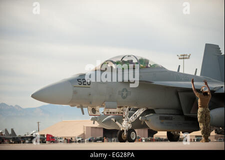 La Marine américaine, le Maître de 3e classe Micah Smith, 135e Escadron d'attaque électronique commandant de bord, Naval Air Station Whidbey Island, Washington, ordonne au pilote d'un EA-18G Growler hors d'une place de stationnement avant d'une mission de formation le 29 janvier 2014, à Nellis Air Force Base. Nevada Le Boeing EA-18G Growler est un porte-avions de guerre électronique, une version spécialisée de la deux places F/A-18F Super Hornet. Drapeau rouge donne aux équipages et les opérations de soutien aérien militaires de diverses cellules, les services militaires et les pays alliés l'occasion d'intégrer la pratique et lutter contre le pupitre Banque D'Images