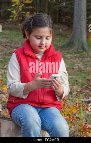 Cute kid, une fille, jouant avec un téléphone intelligent dans la forêt. Exemple d'influence de la technologie sur les enfants et nos vies. Banque D'Images