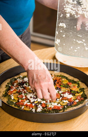 Femme, frais râpé saupoudrer de fromage mozzarella sur un végétarien multi-grains, des pizzas à pâte épaisse Banque D'Images