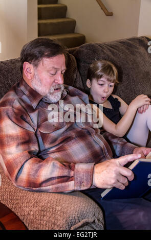 La lecture de son grand-père Sixtyish six ans petite fille qui est l'expression de surprise à ce qu'elle entend Banque D'Images