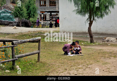 BU00140-00...BHOUTAN - Deux jeunes garçons en costume traditionnel faire un peu de l'étude de dernière minute dans la cour de l'école rurale. Banque D'Images