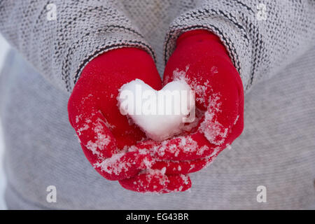 Gants rouge tenant un cœur fait de la neige Banque D'Images