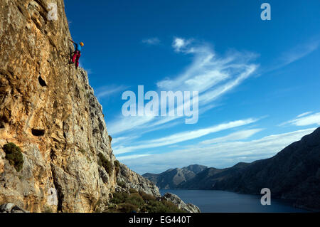 Rock climber mature sur falaise ensoleillée avec des nuages cirrus Banque D'Images