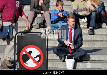 Londres, Angleterre, Royaume-Uni. L'homme de manger sur les marches de la National Gallery à Trafalgar Square. 'Ne pas nourrir les pigeons' sign Banque D'Images