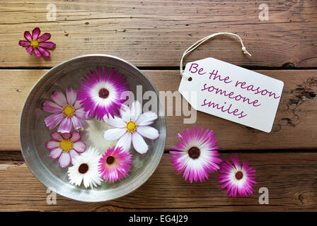 Bol en argent avec une étiquette avec la vie Citation être la raison pour laquelle quelqu'un sourit avec Mauve et blanc Cosmea fleurs sur fond de bois V Banque D'Images