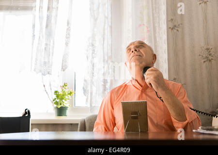 Vieil homme assis en orange shirt le rasage des poils sur son cou à l'aide de rasoirs électriques tout en étant orienté vers le haut Banque D'Images