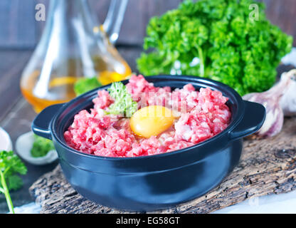 La viande hachée et oeufs crus dans un bol et sur une table Banque D'Images