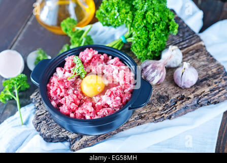 La viande hachée et oeufs crus dans un bol et sur une table Banque D'Images