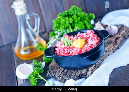 La viande hachée et oeufs crus dans un bol et sur une table Banque D'Images