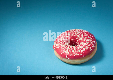 Donut avec glaçage rouge isolé sur fond bleu avec copyspace Banque D'Images