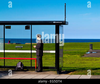 Jeune homme de répondre à l'attente à un arrêt de bus avec la mer derrière à Whitley Bay North Tyneside, Tyne et Wear England UK Banque D'Images