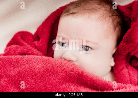 Beau 3 mois bébé couché sur un lit recouvert d'une couverture rouge. Portrait doux Banque D'Images