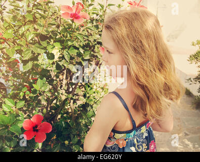 Belle petite fille se tient sur fond de fleurs en plein air Banque D'Images