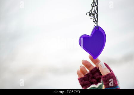 Femme dans les mains des mitaines pour atteindre le purple heart against a white background bokeh Banque D'Images